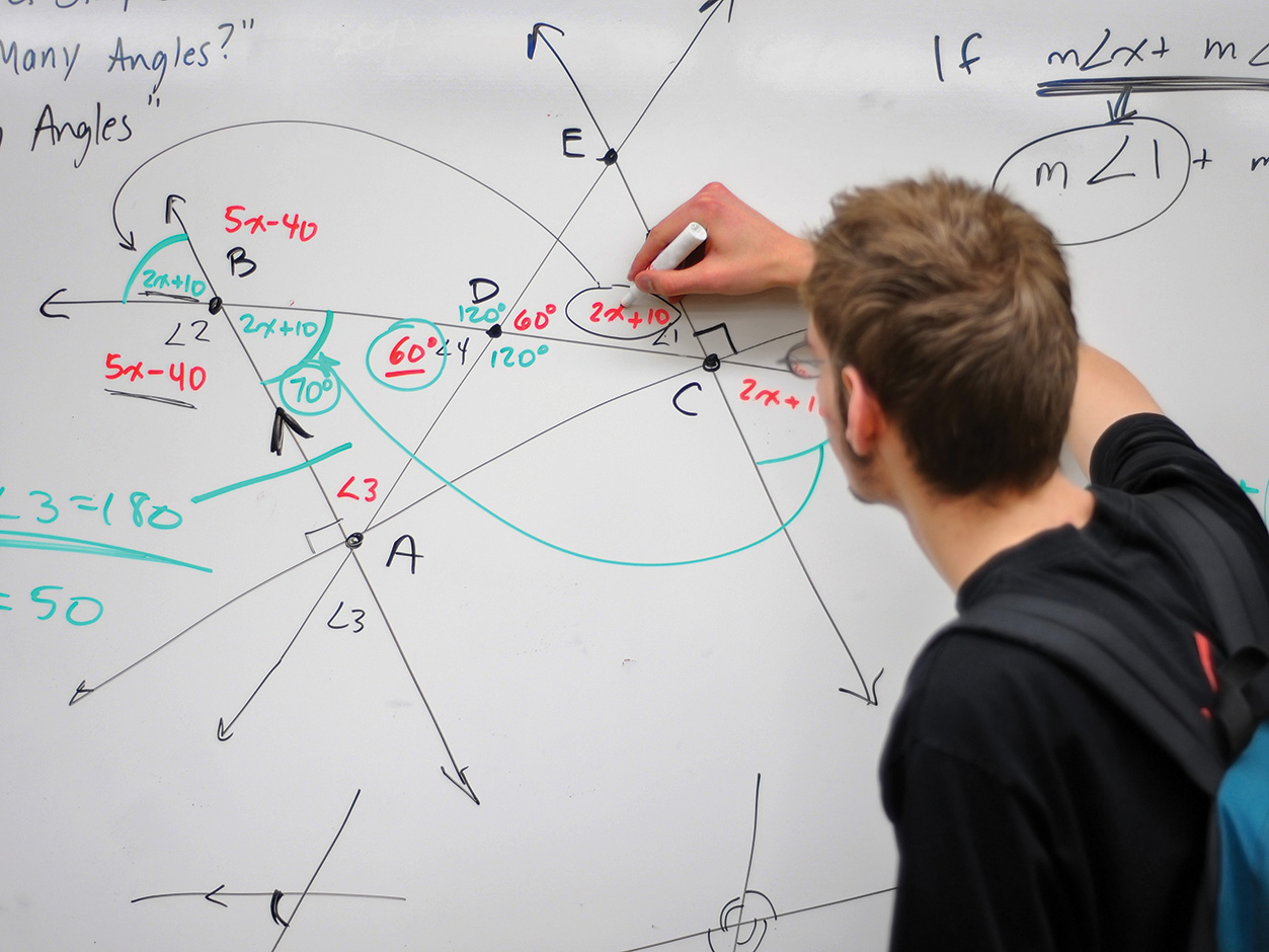 A student writing a math equation on a whiteboard