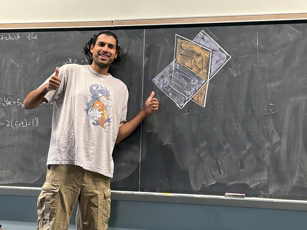 Rayan Ibrahim stands in front of a chalkboard with intersecting rectangles drawn in chalk